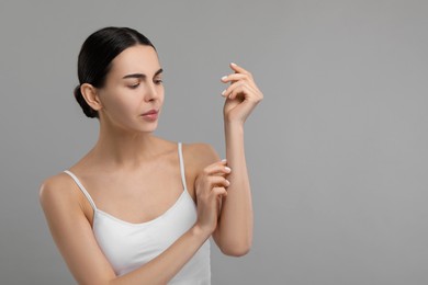 Photo of Woman with dry skin checking her arm on gray background, space for text