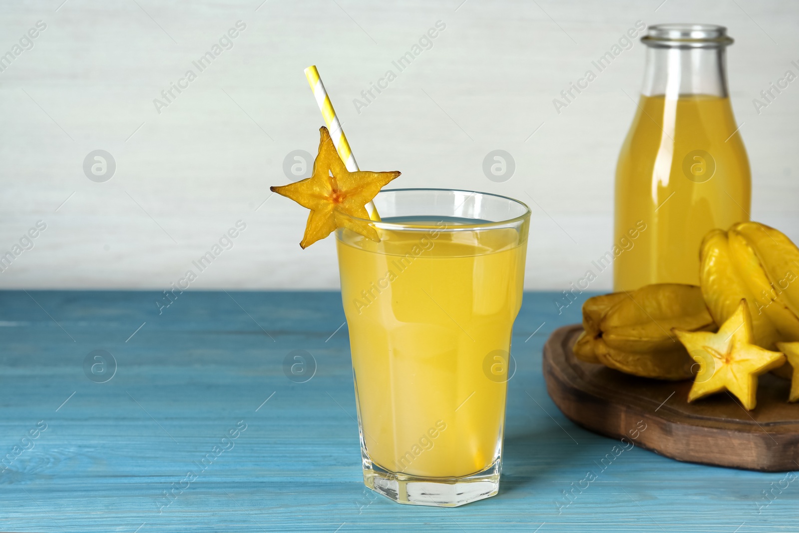 Photo of Delicious carambola juice and fresh fruits on light blue wooden table. Space for text