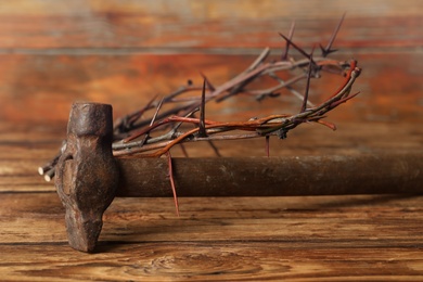 Photo of Crown of thorns and hammer on wooden table. Easter attributes