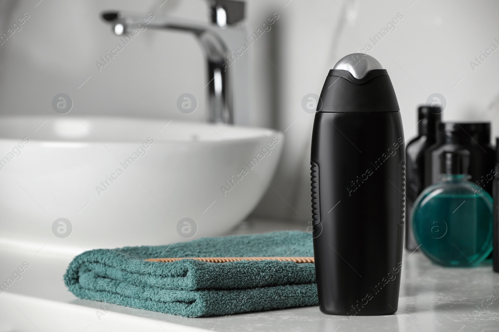 Photo of Bottle of shampoo and towel near sink on bathroom counter, space for text