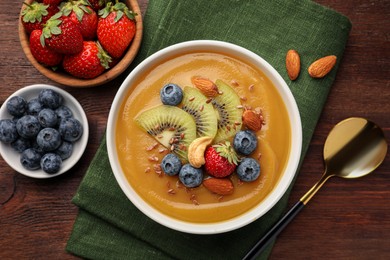Photo of Delicious smoothie bowl with fresh berries, kiwi and nuts on wooden table, flat lay