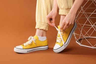 Photo of Woman tying shoelace of classic old school sneaker on brown background, closeup
