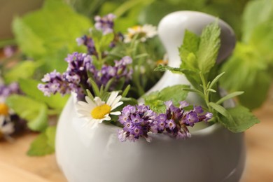 Photo of Mortar with fresh lavender, chamomile flowers, herbs and pestle on blurred background, closeup