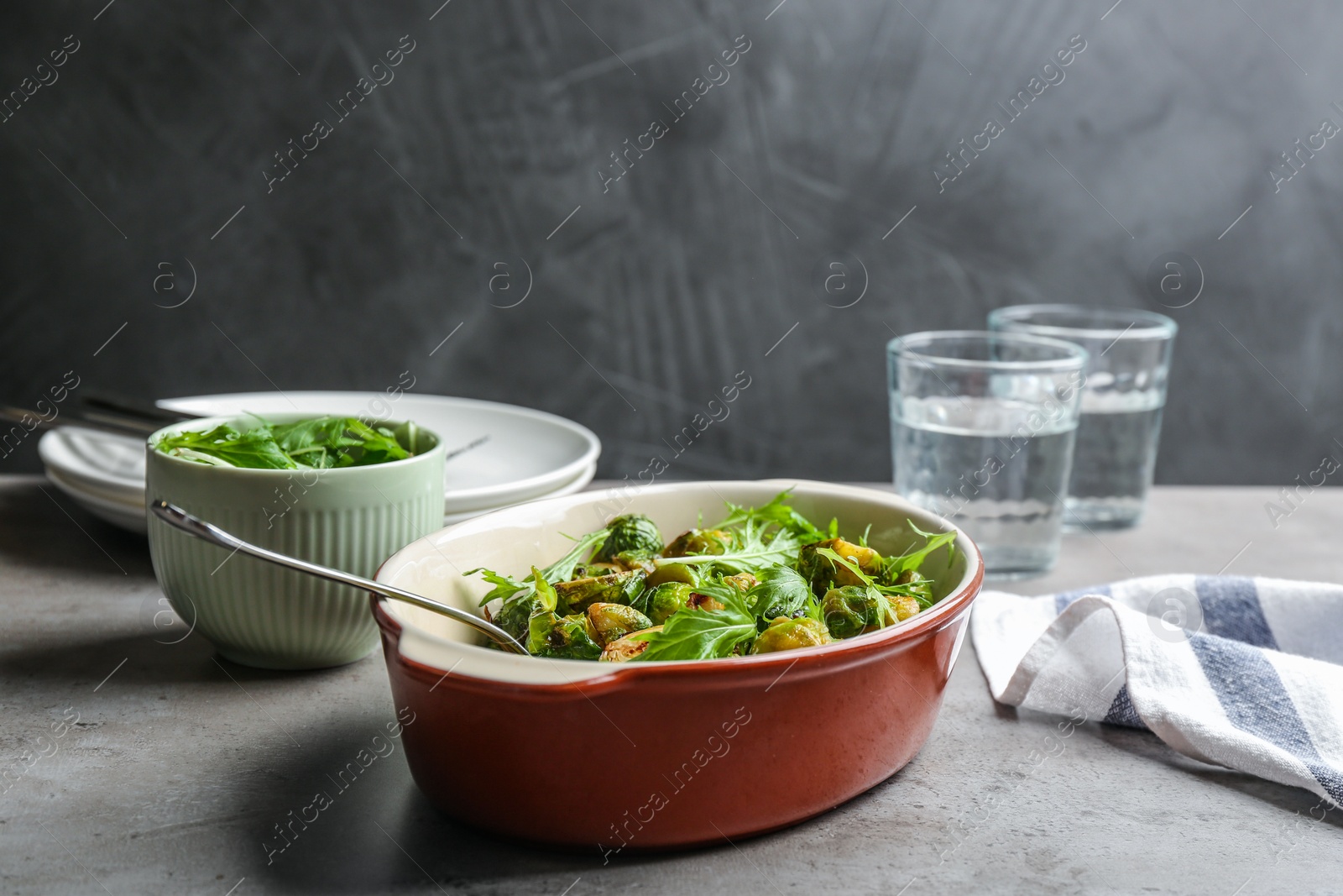 Photo of Roasted Brussels sprouts with arugula in baking dish on grey table