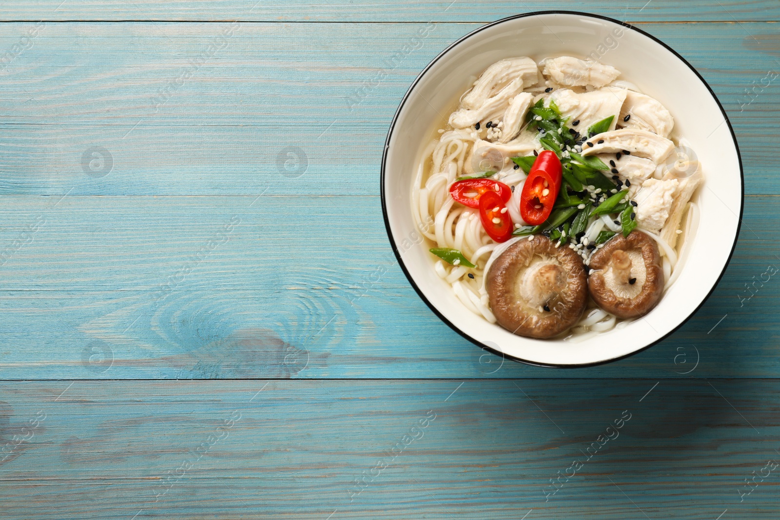 Photo of Delicious ramen with meat and mushrooms in bowl on light blue wooden table, top view. Space for text