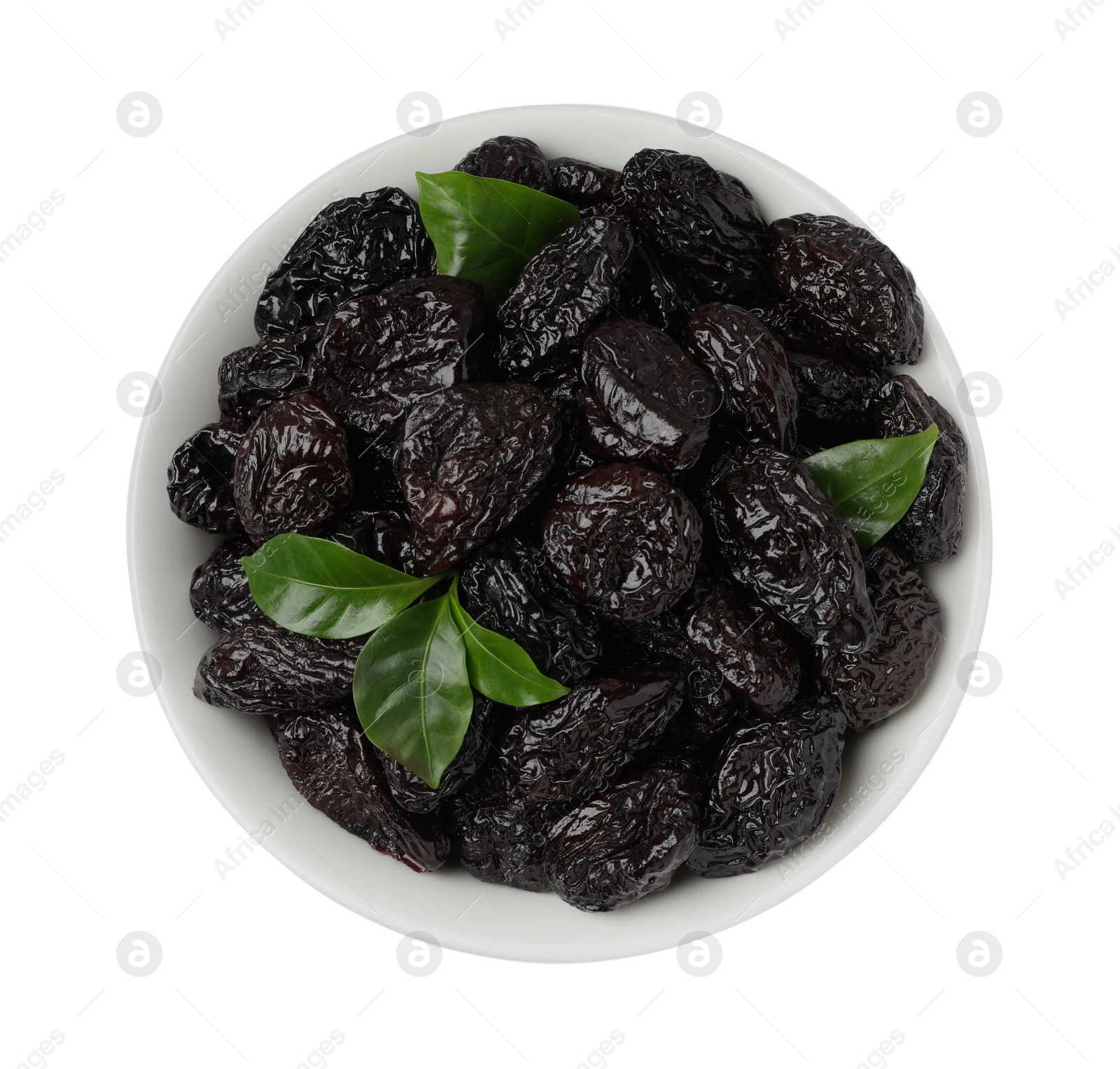 Photo of Bowl with sweet dried prunes and green leaves isolated on white, top view