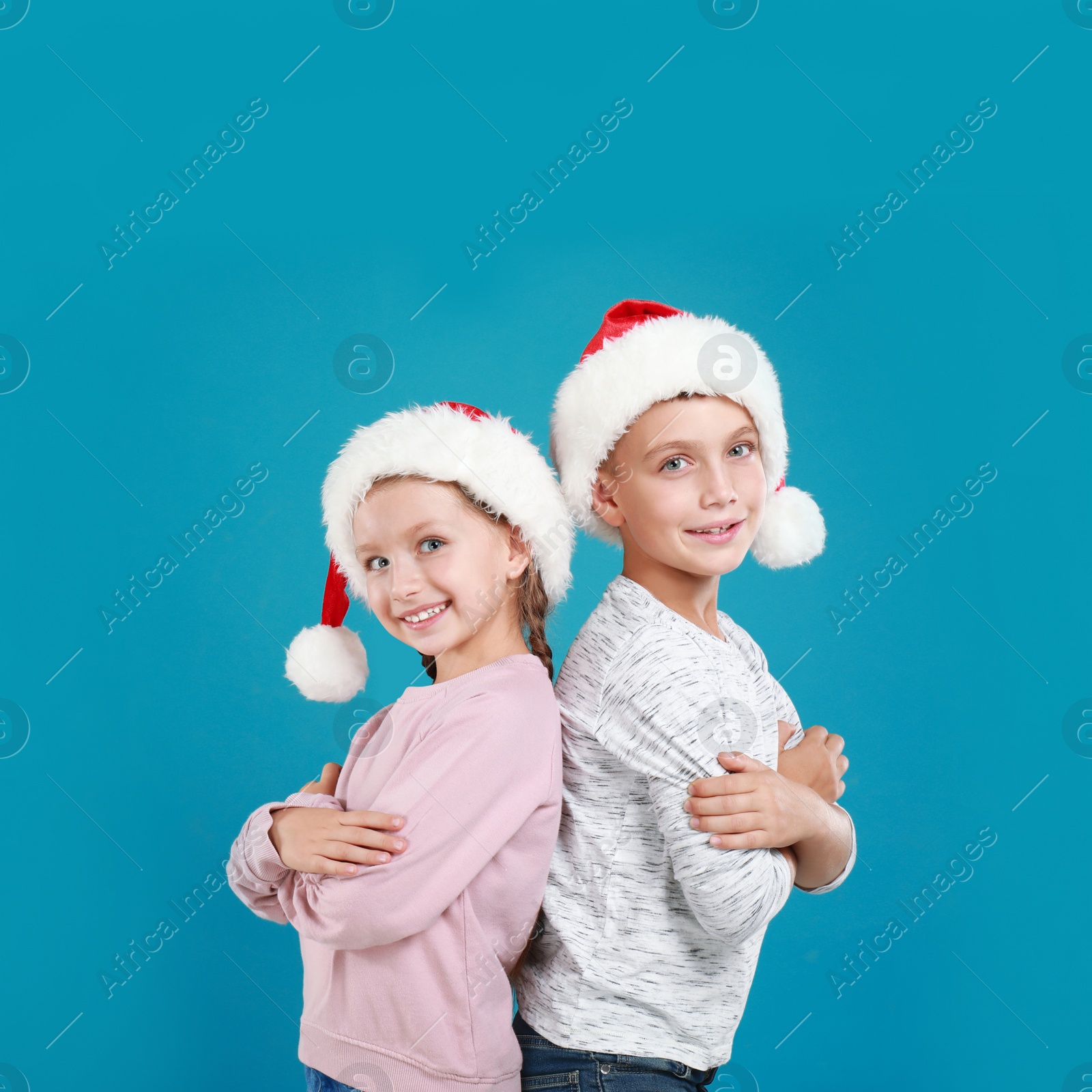 Image of Happy little children in Santa hats on light blue background. Christmas celebration