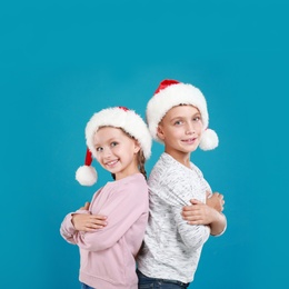 Image of Happy little children in Santa hats on light blue background. Christmas celebration