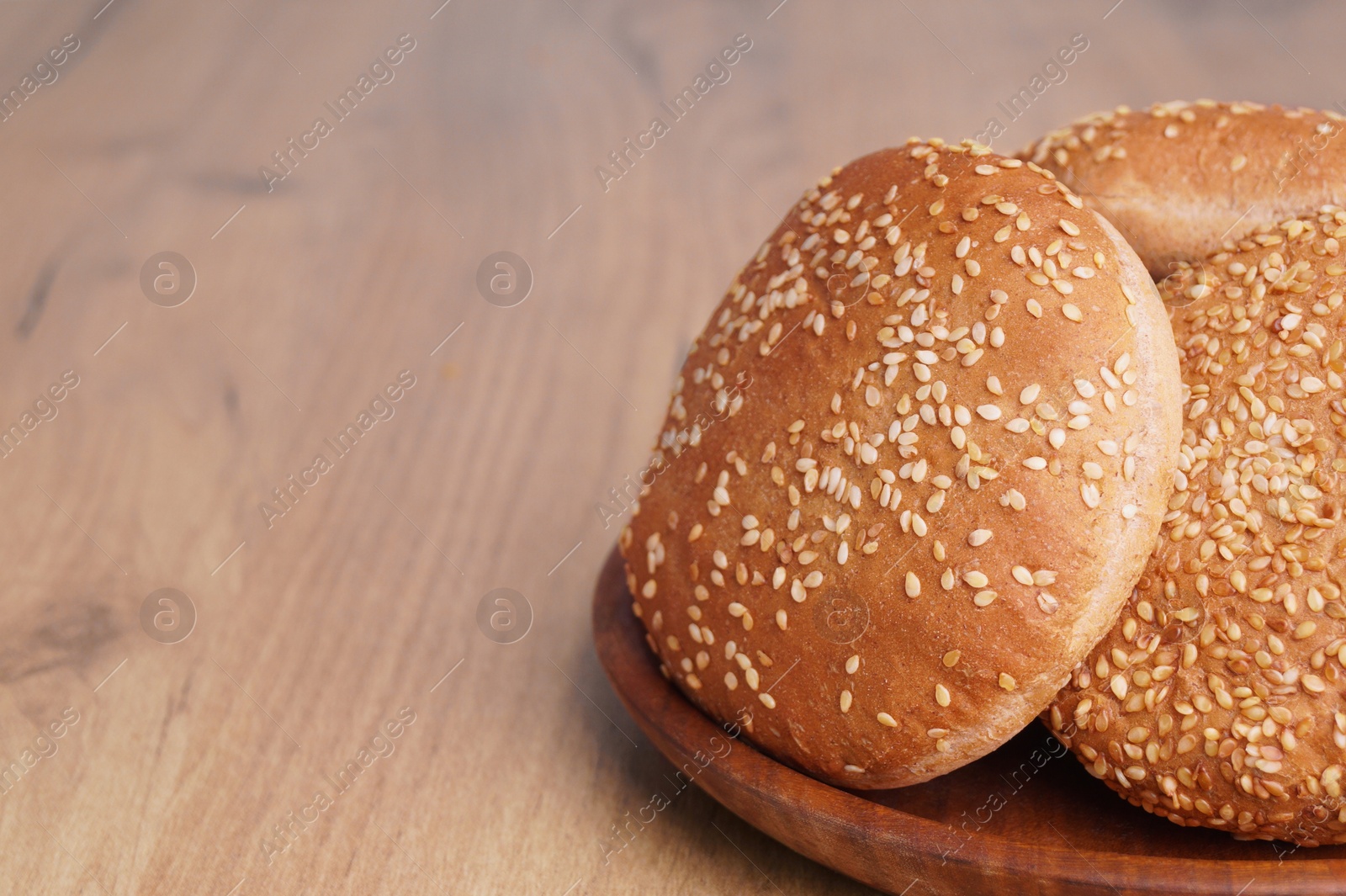 Photo of Fresh buns with sesame seeds on wooden table. Space for text