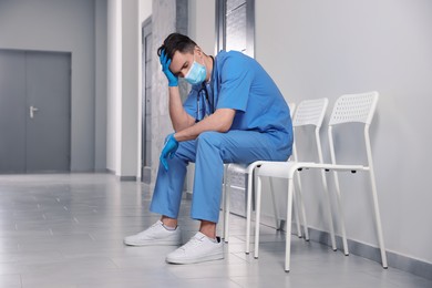 Photo of Exhausted doctor sitting on chair in hospital hallway