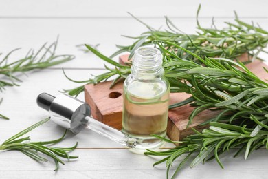 Fresh green rosemary and bottle of essential oil on white wooden table, space for text