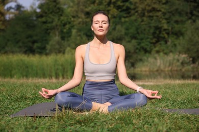 Beautiful woman practicing yoga on mat outdoors. Lotus pose