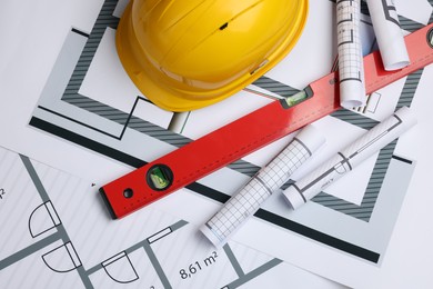 Photo of Construction drawings, safety hat and bubble level on house plan, flat lay