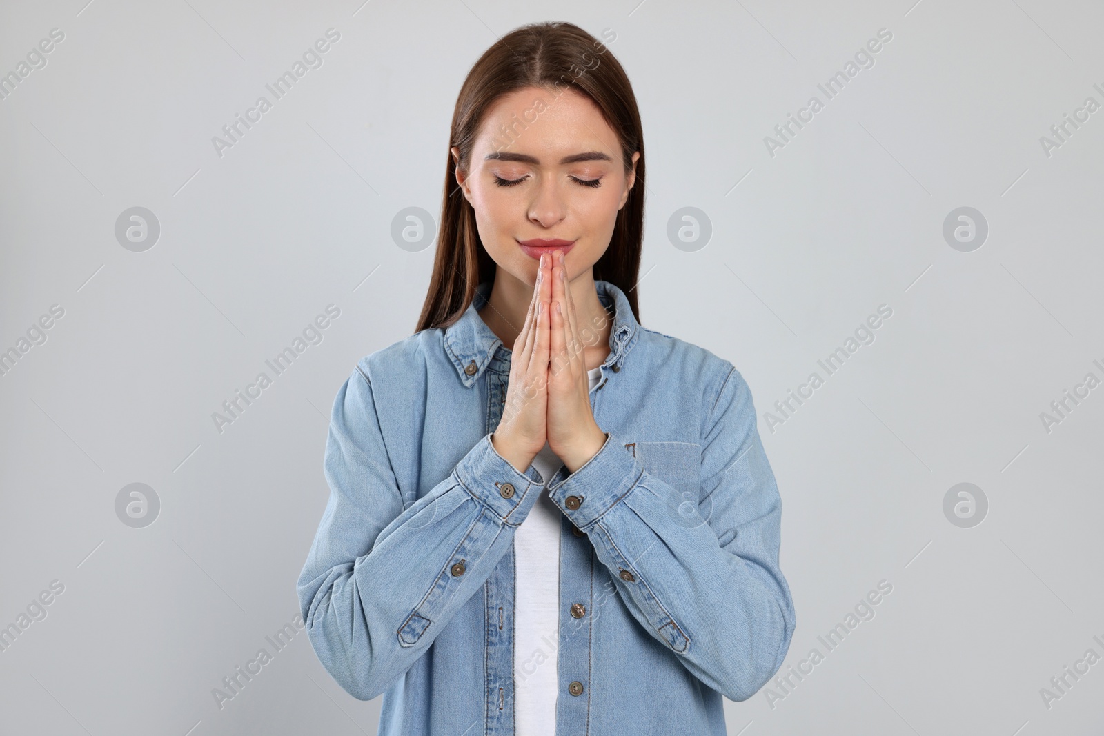 Photo of Woman with clasped hands praying on light grey background