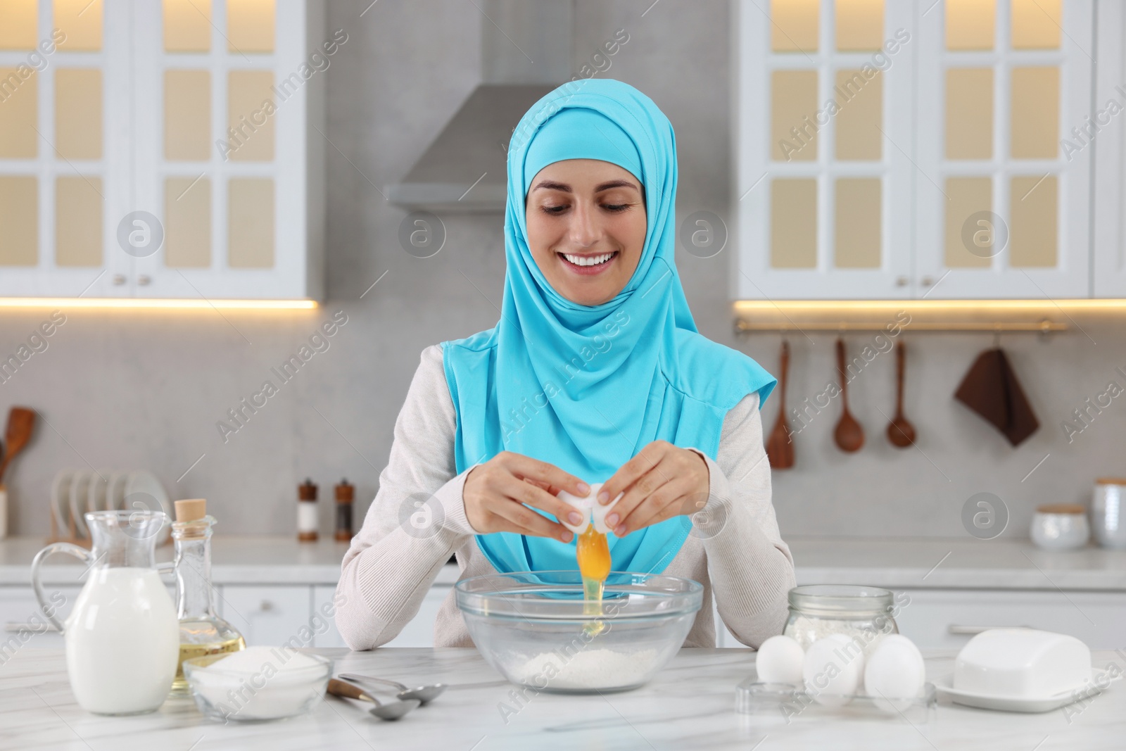 Photo of Muslim woman making dough at white table in kitchen