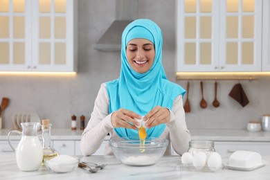 Muslim woman making dough at white table in kitchen