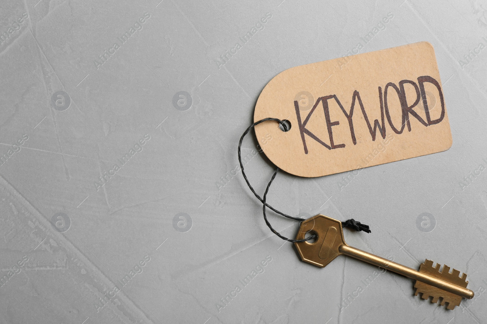 Photo of Key with tag KEYWORD on grey background, top view. Space for text