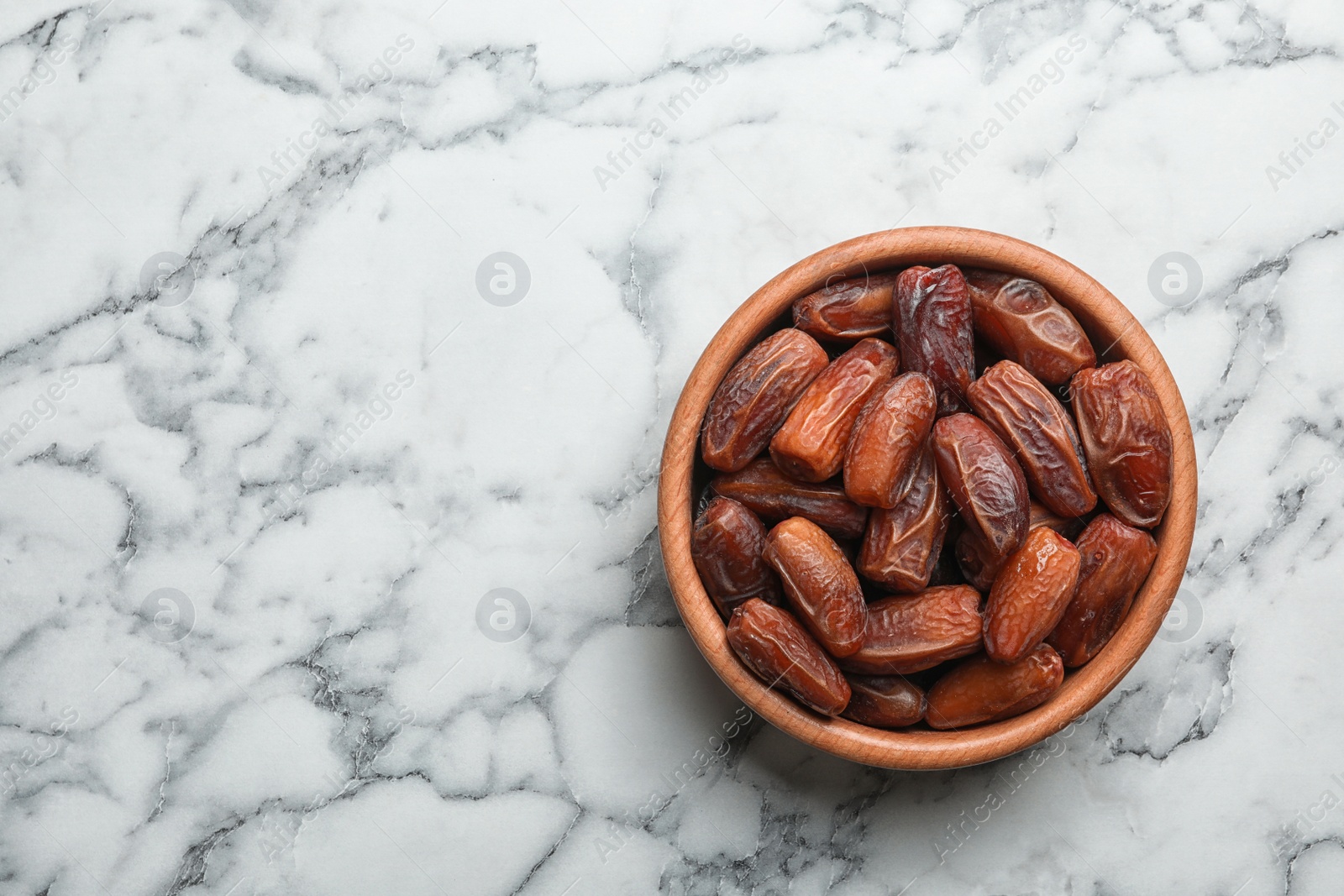 Photo of Bowl with sweet dried date fruits on marble background, top view. Space for text