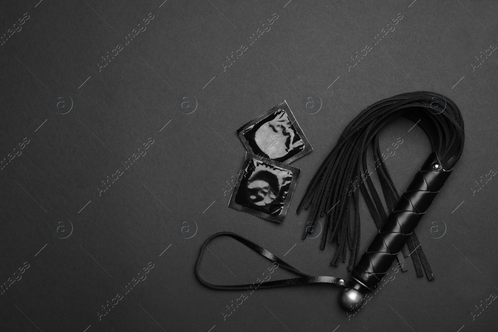 Photo of Whip and condoms on black background, top view with space for text. Sex game