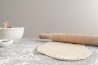 Photo of Fresh dough and rolling pin on light grey table. Cooking grissini