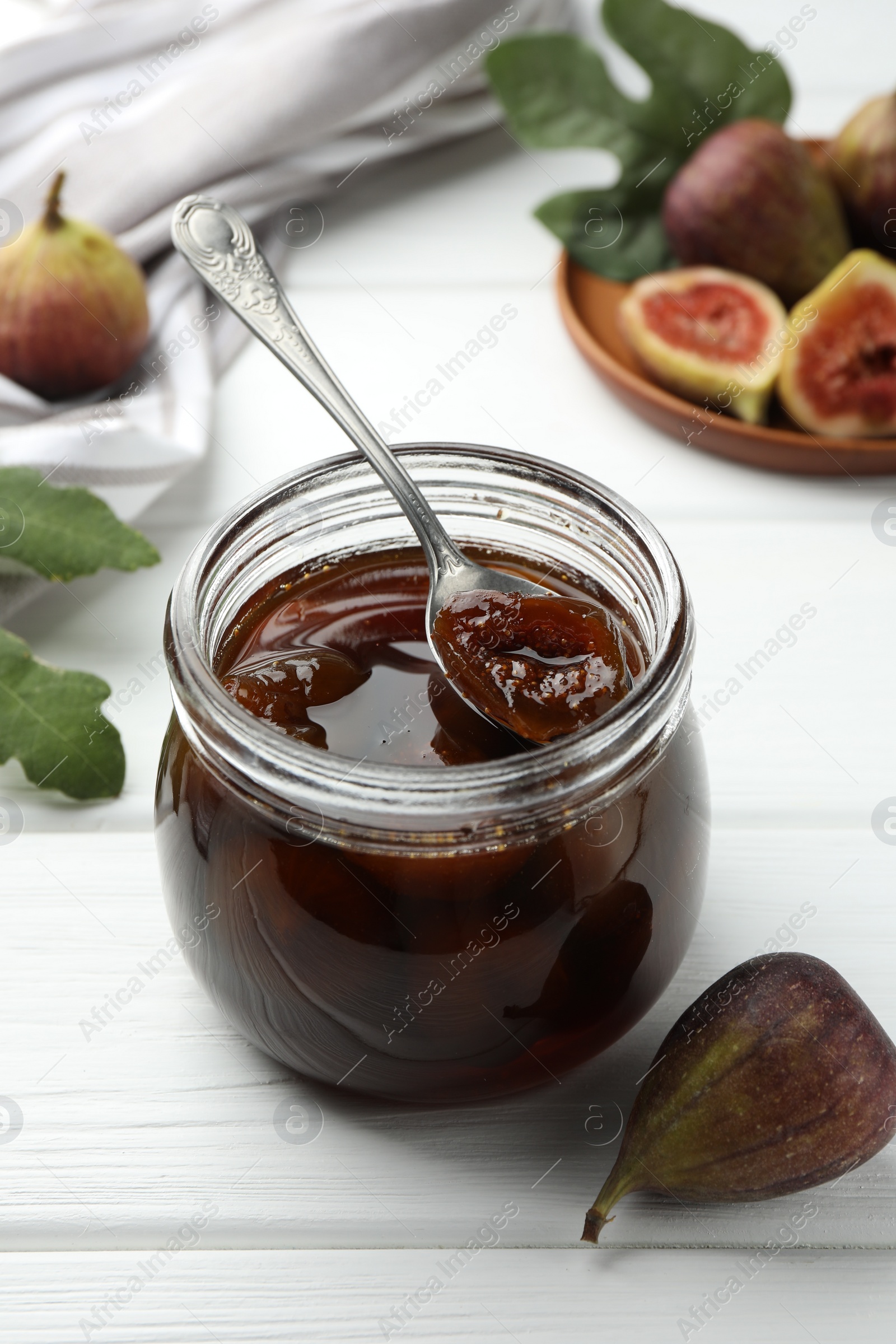 Photo of Jar of tasty sweet jam and fresh figs on white wooden table