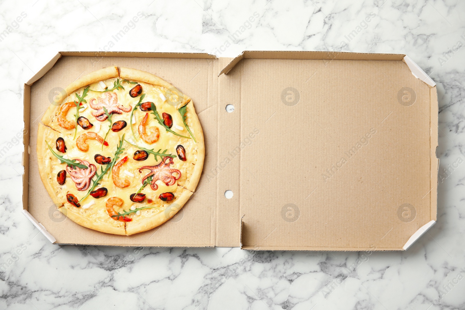 Photo of Delicious seafood pizza in cardboard box on white marble table, top view