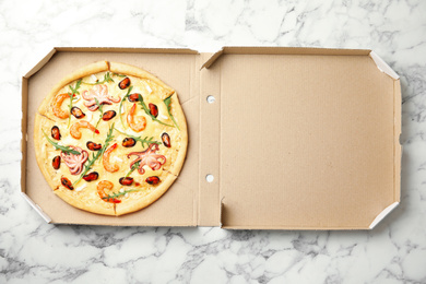 Delicious seafood pizza in cardboard box on white marble table, top view