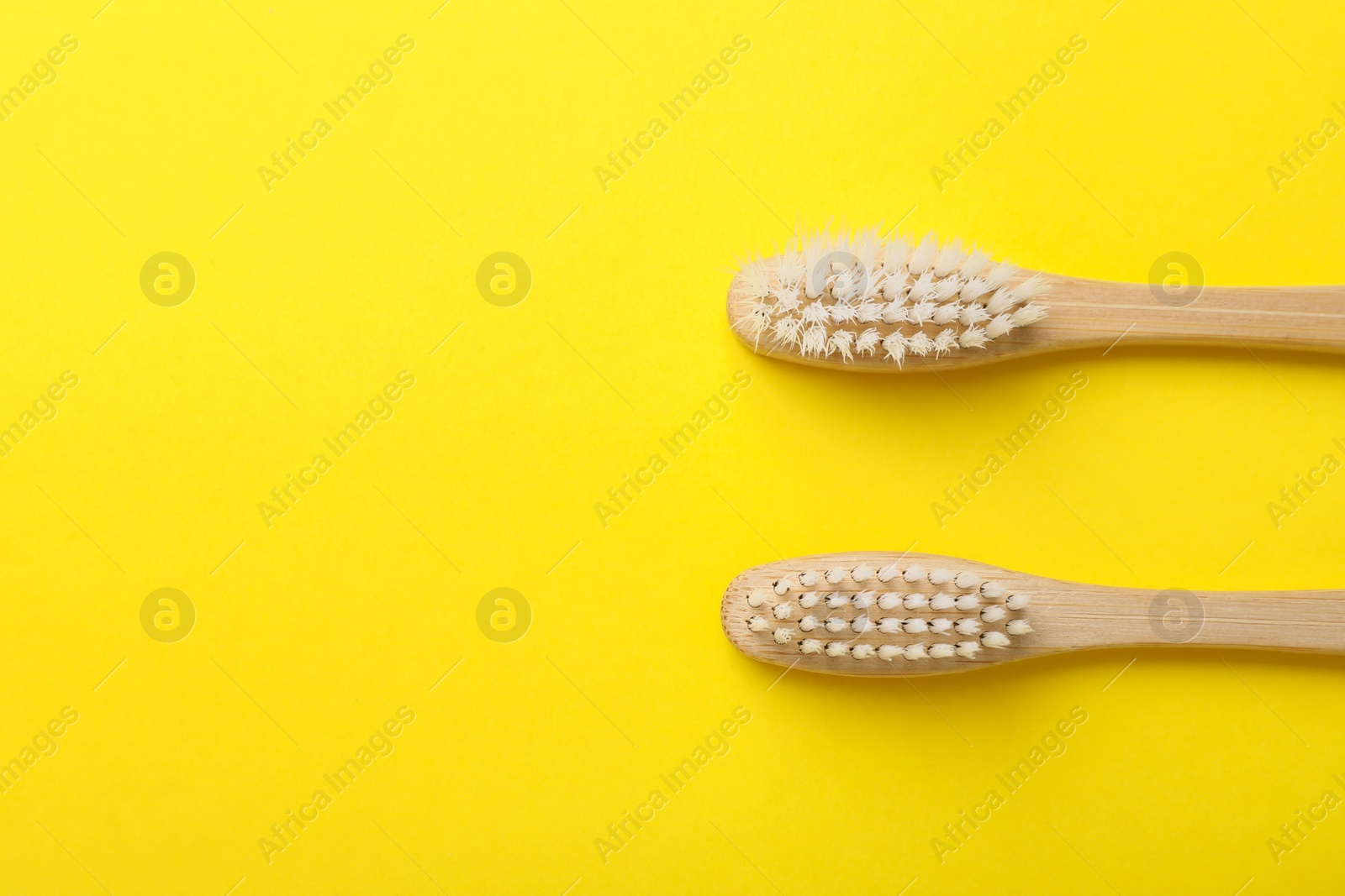 Photo of Bamboo toothbrushes on yellow background, flat lay. Space for text