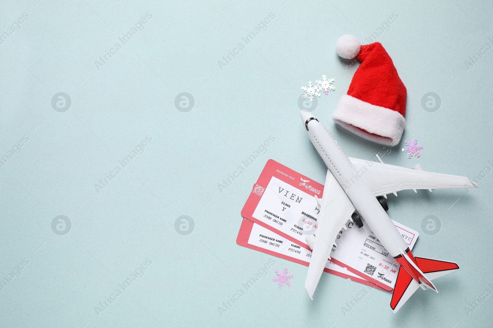 Photo of Santa hat, toy airplane and airline tickets on light blue background, space for text. Christmas vacation