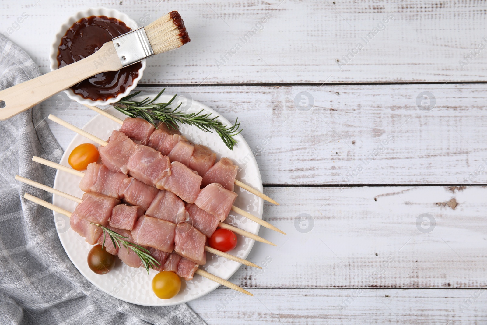 Photo of Skewers with pieces of raw meat, rosemary, tomatoes and marinade on rustic wooden table. Space for text