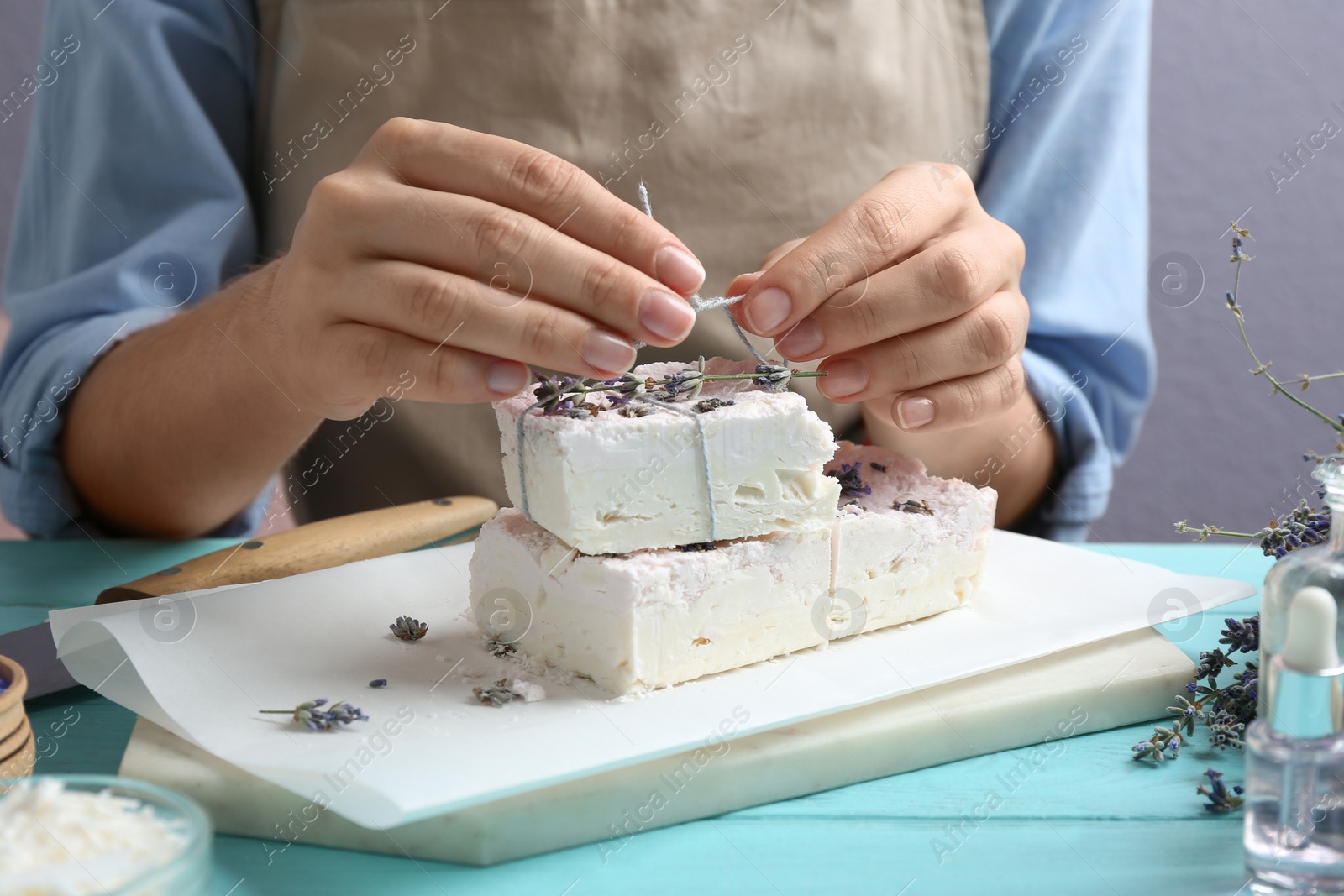 Photo of Woman decorating hand made soap bars with lavender flowers at light blue wooden table, closeup