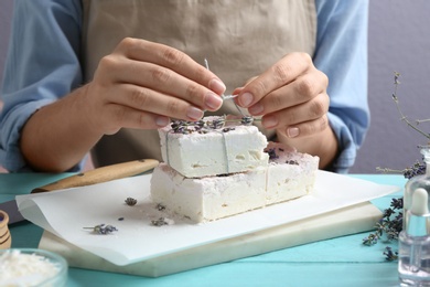 Photo of Woman decorating hand made soap bars with lavender flowers at light blue wooden table, closeup