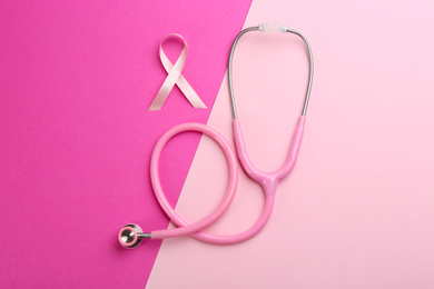 Photo of Pink ribbon as breast cancer awareness symbol and stethoscope on color background, flat lay