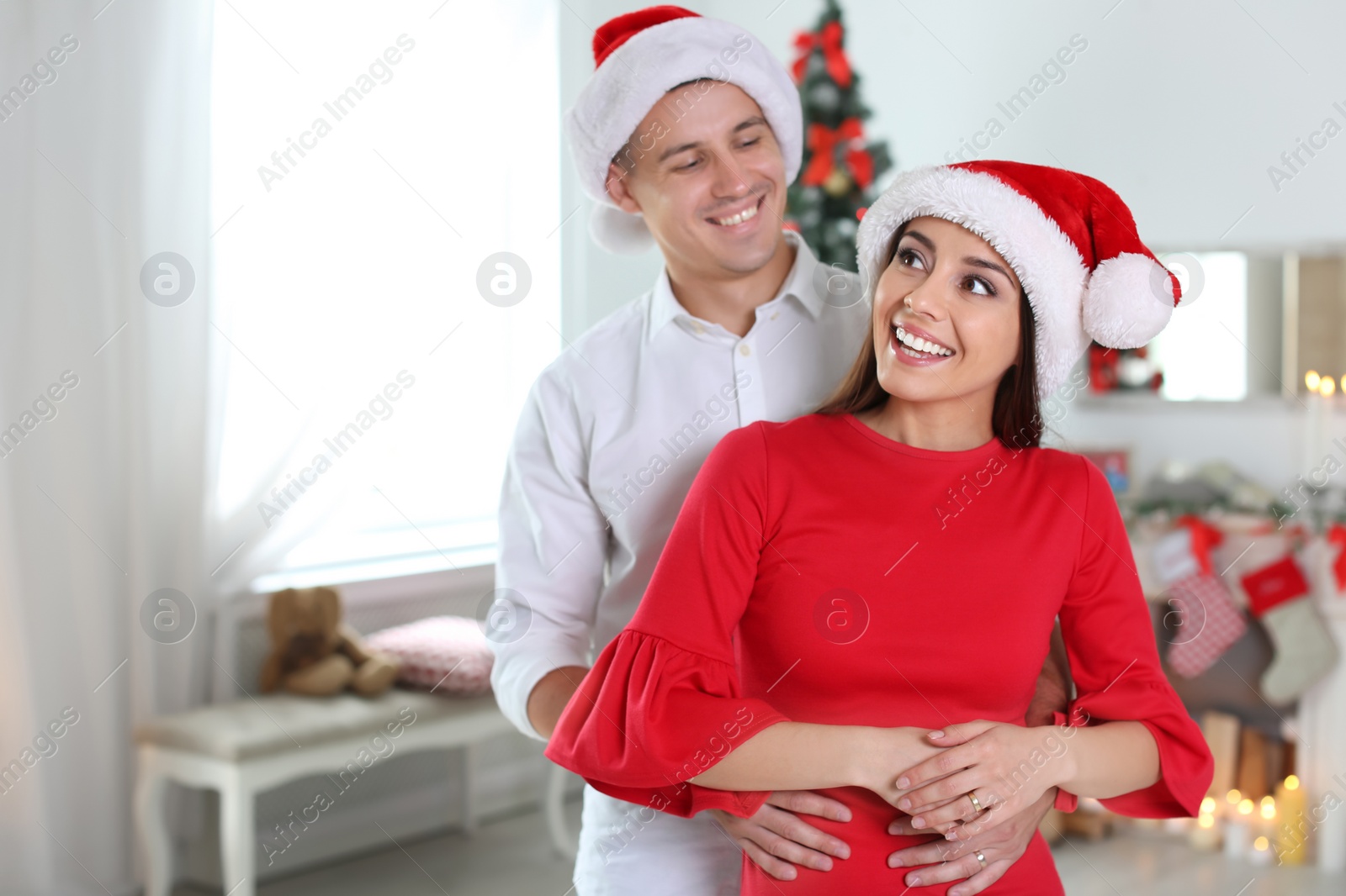 Photo of Happy young couple in Santa hats celebrating Christmas at home