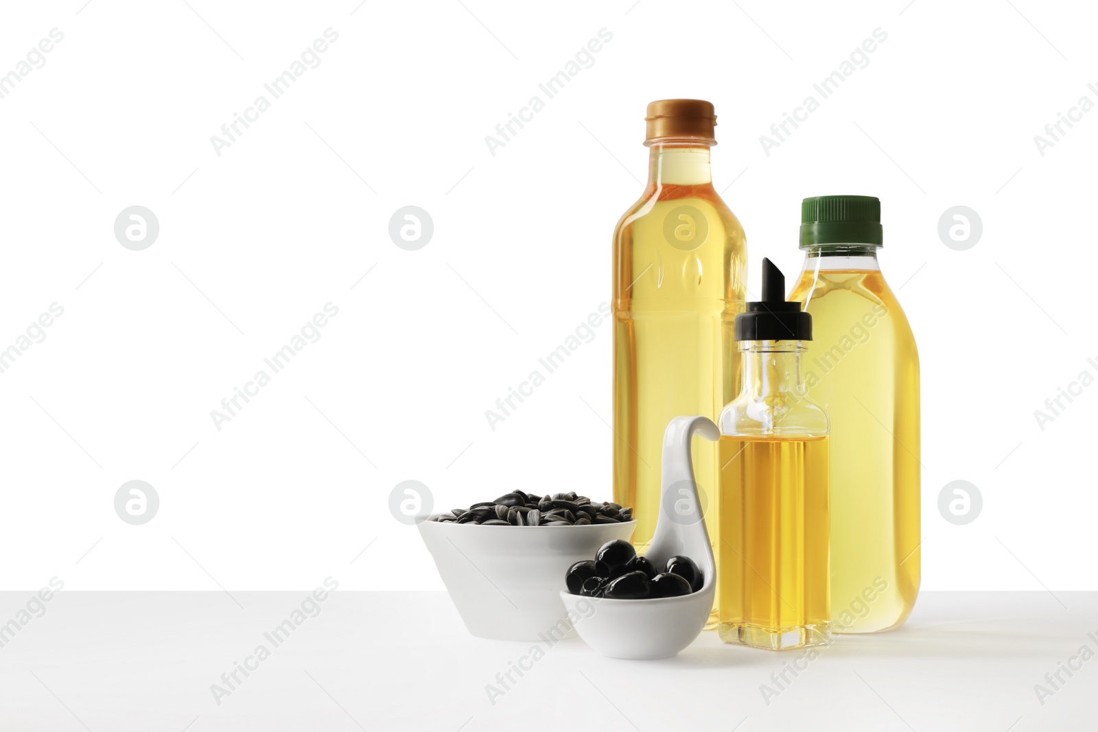 Photo of Bottles of different cooking oils, olives and sunflower seeds on white background, space for text