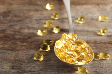 Spoon with cod liver oil pills on table, closeup