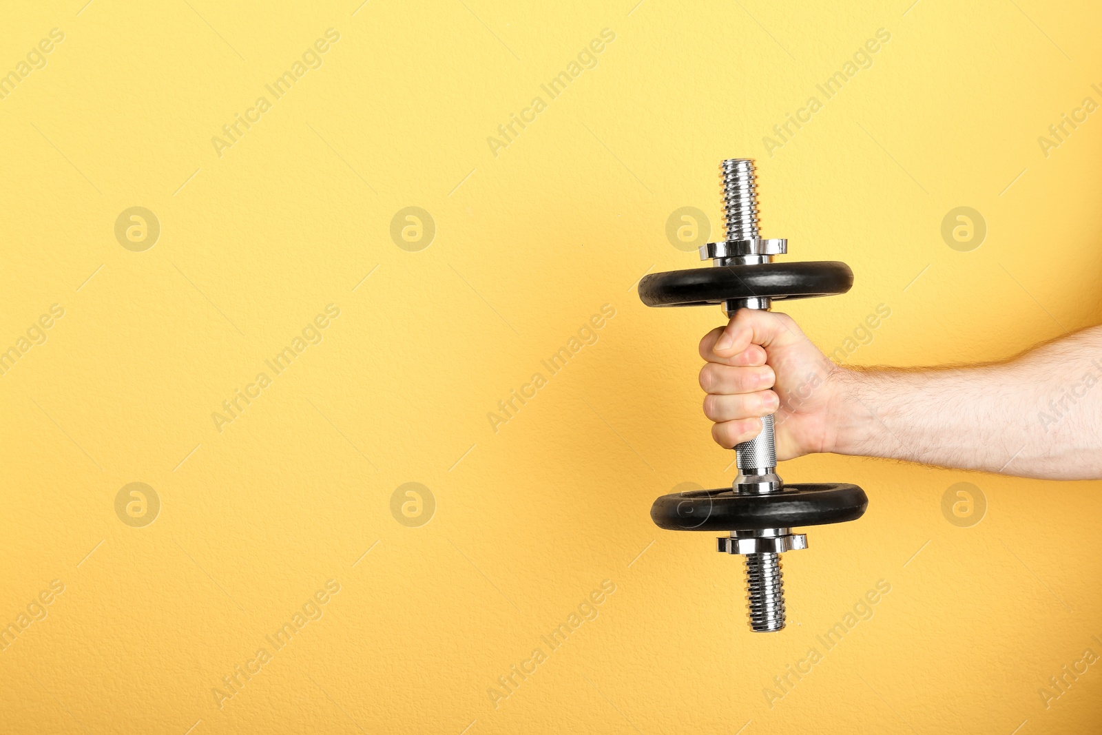 Photo of Male athlete holding metal dumbbell on color background. Space for text