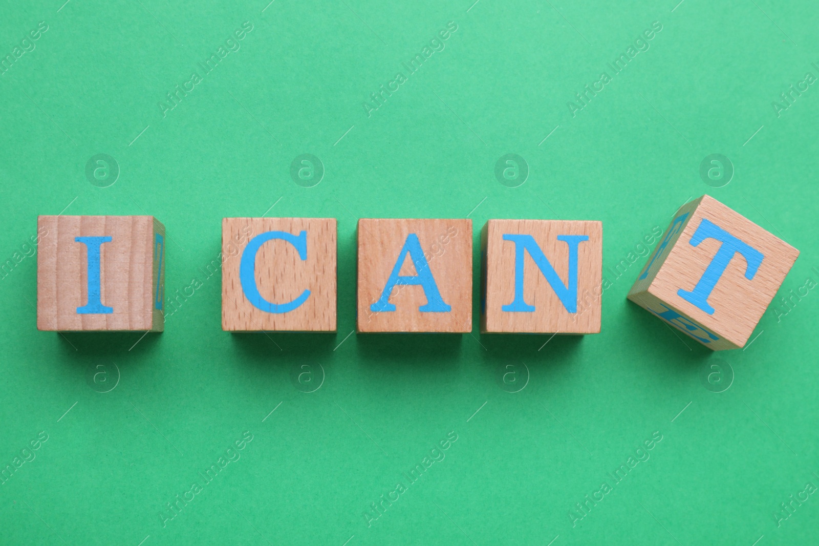 Photo of Motivation concept. Changing phrase from I Can't into I Can by removing wooden cube with letter T on green background, top view