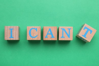 Photo of Motivation concept. Changing phrase from I Can't into I Can by removing wooden cube with letter T on green background, top view