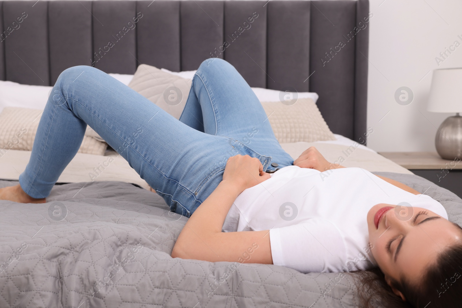 Photo of Woman trying to put on tight jeans on bed at home