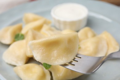 Photo of Delicious dumpling (varenyk) with cottage cheese on fork over plate, closeup
