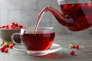 Photo of Pouring hot cranberry tea into glass cup and fresh berries on light grey textured table, closeup