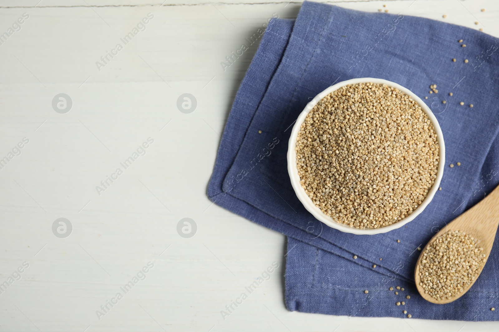 Photo of Bowl and spoon with quinoa on white wooden table, flat lay. Space for text