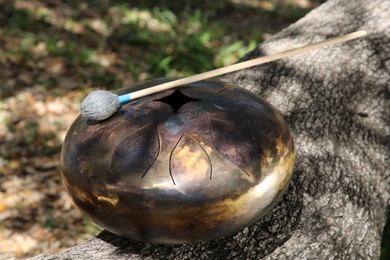 Photo of Steel tongue drum with mallet on tree bark outdoors. Percussion musical instrument