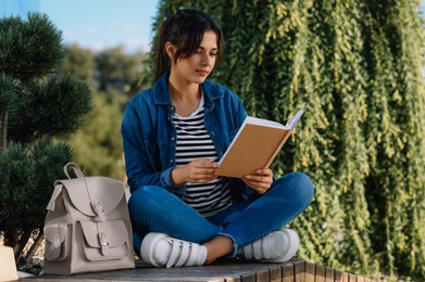 Young woman reading book on bench outdoors