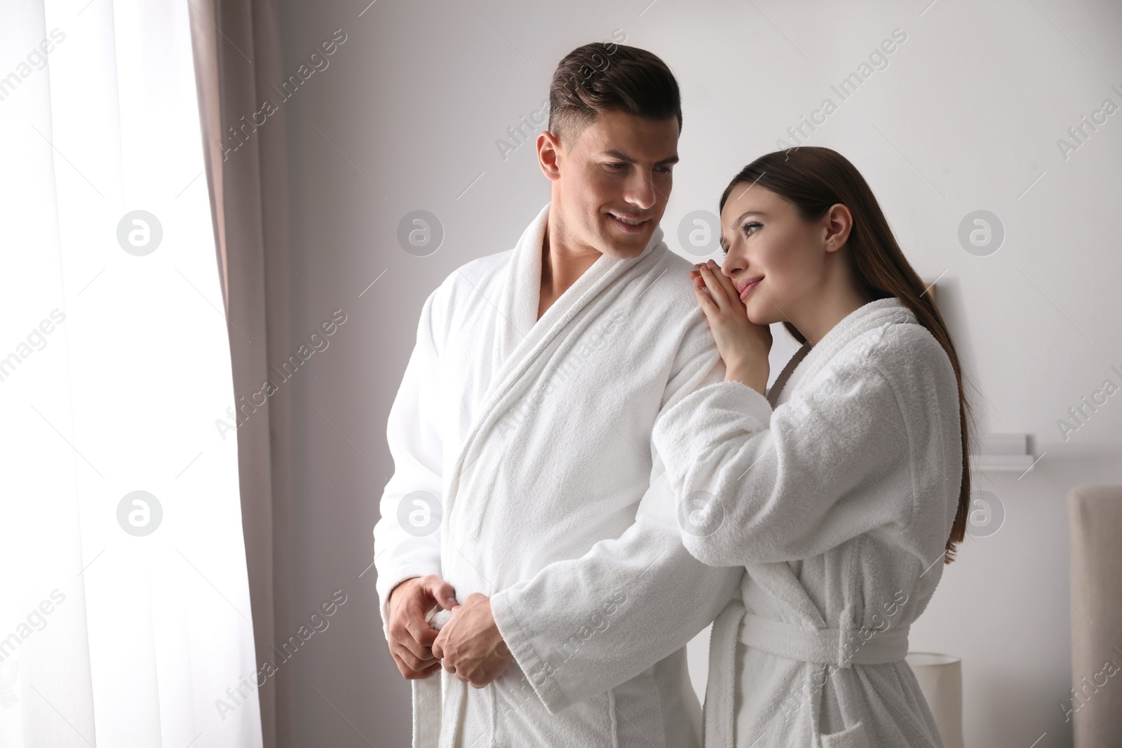 Photo of Happy couple wearing bathrobes near window in room