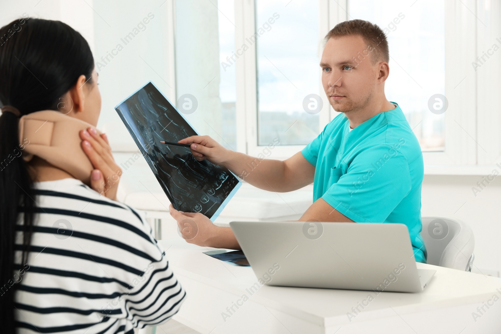 Photo of Doctor with neck MRI image consulting patient in clinic