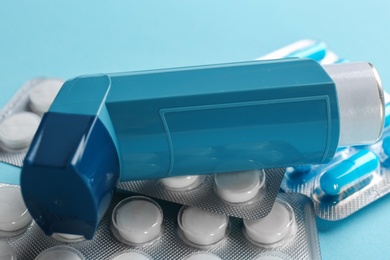 Photo of Asthma inhaler and pills on color background, closeup