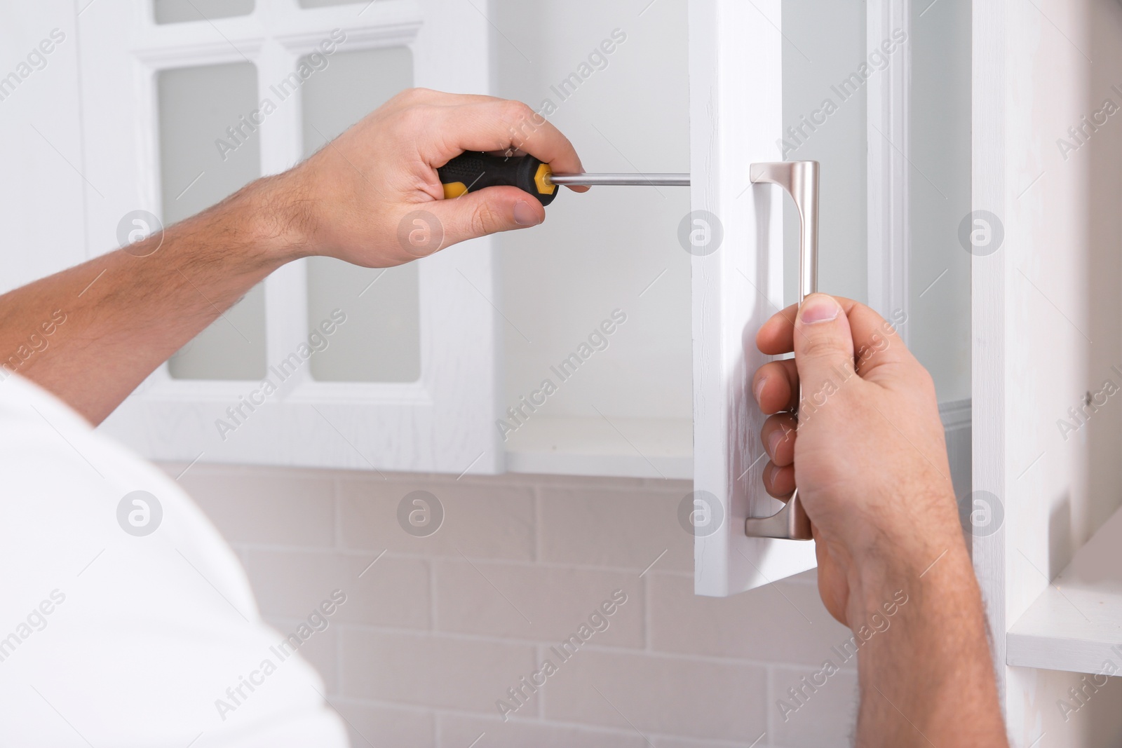 Photo of Worker installing handle of cabinet door with screwdriver in kitchen, closeup