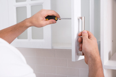 Worker installing handle of cabinet door with screwdriver in kitchen, closeup